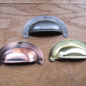 May include: Three metal drawer pulls in different finishes: silver, copper, and gold. Each pull is a half-circle shape with a slight curve in the center.