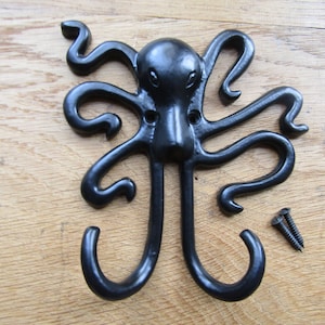 May include: Black metal octopus hook with two hooks. The octopus has a detailed face and eight tentacles. The hook is mounted on a wooden surface with two screws.