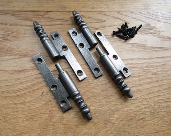 May include: Two pairs of antique-style, black iron hinges with decorative, twisted finials. The hinges are laid out on a wooden surface with a pile of screws.