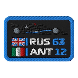 Könnte beinhalten: Ein schwarzer und blauer gestickter Aufnäher mit einem stilisierten Bild eines Rennwagens, dem Text "RUS 63" und dem Text "ANT 12". Der Aufnäher zeigt die Flaggen von Großbritannien und Italien.