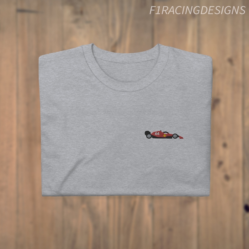 May include: A grey t-shirt with a small embroidered image of a red racing car with the number 14 on the side.