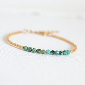 Puede incluir: Un delicado brazalete de cadena dorada con una fila de cuentas turquesa.