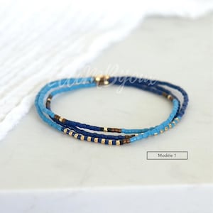 May include: A multi-strand beaded bracelet with blue, gold, and brown beads. The bracelet is layered with different shades of blue beads, creating a gradient effect. The bracelet is labeled "Mod&egrave;le 1".