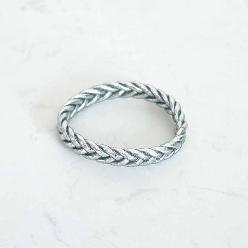 on peut voir un bracelet jonc forme tressé couleur argent pour femme, sur d'autres photos il est accumulé sur un poignet avec des joncs fin, épais et torsadé