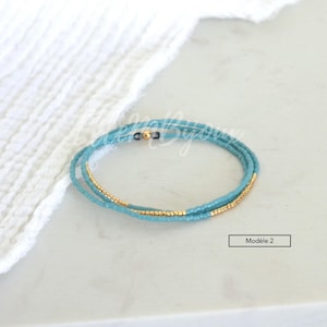 May include: A turquoise and gold beaded bracelet with a clasp. The bracelet is on a white surface.  Mod&egrave;le 2