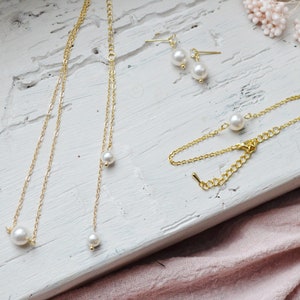 Puede incluir: Un conjunto de joyas de oro que incluye un delicado collar con tres acentos de perlas, una pulsera con un solo acento de perla y un par de pendientes de perlas.