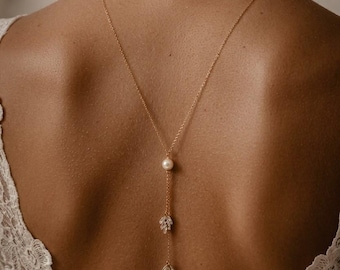 May include: A gold-toned lariat necklace featuring a single white pearl accent and two dangling leaf-shaped charms adorned with clear crystals. The delicate chain hangs down the center of the back, suspended from a simple gold-toned chain.