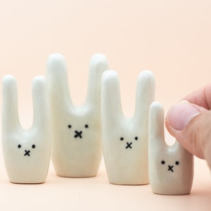 May include: Five white ceramic bunny figurines with black eyes and a black X for a mouth. The bunnies are arranged in a row from largest to smallest.