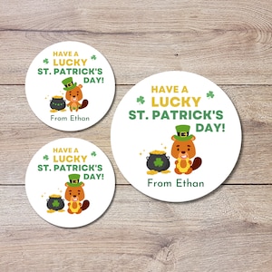 Puede incluir: Tres pegatinas redondas con un castor de dibujos animados que lleva un sombrero verde y sostiene una herradura. Las pegatinas dicen "Have a Lucky St. Patrick's Day!" y "From Ethan".