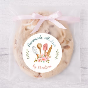Puede incluir: Pegatina redonda con fondo blanco y texto turquesa que dice "Homemade with Love by Christina". La pegatina presenta una ilustraci&oacute;n de acuarela de utensilios de cocina, incluyendo un batidor, una cuchara de madera, una esp&aacute;tula y un rodillo, rodeados de flores rosas.