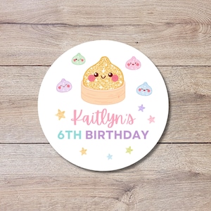 May include: A round white sticker featuring a central illustration of a gold glittery dumpling in a bamboo steamer, surrounded by smaller colorful dumpling characters and stars. The text reads "Kaitlyn's 6TH BIRTHDAY" in pink and purple.