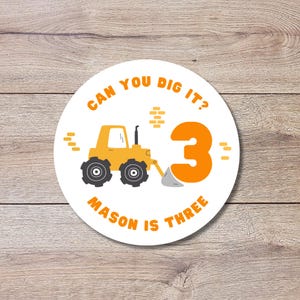May include: A circular sticker featuring a yellow construction tractor, a large orange number 3, and the text CAN YOU DIG IT? and MASON IS THREE in orange font. The design includes small orange brick icons on a white background.