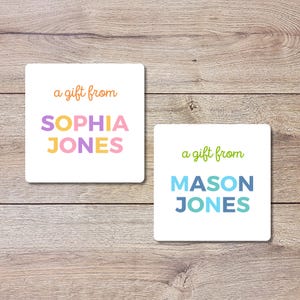 May include: Two white square gift tags with text on a wooden background. One tag reads "a gift from SOPHIA JONES" in colorful letters. The other tag says "a gift from MASON JONES" in blue and green letters.