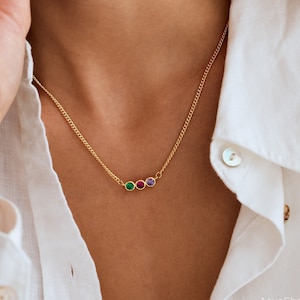Könnte beinhalten: Eine goldene Kettenkette mit drei kleinen runden Edelsteinen: grün, rot und lila.