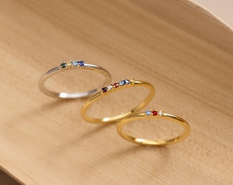May include: Three thin metal rings arranged in a row. The first is silver-toned with four small multicolored stones. The second is gold-toned with four small multicolored stones. The third is gold-toned with three small multicolored stones.