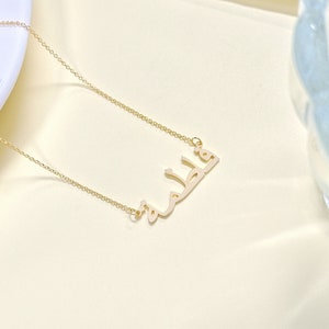 May include: A gold chain necklace with a pendant featuring the Arabic word "Khalid" in a simple, modern font.