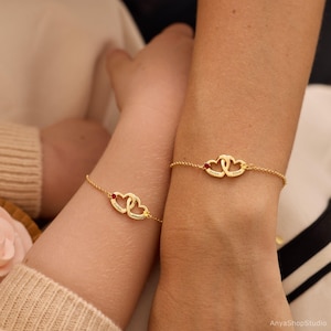 May include: Two gold-toned chain bracelets, each featuring two interlocking heart charms. One heart on each bracelet is accented with a small red stone, and both hearts are engraved with the names Evelyn and Ellen in a delicate script font.