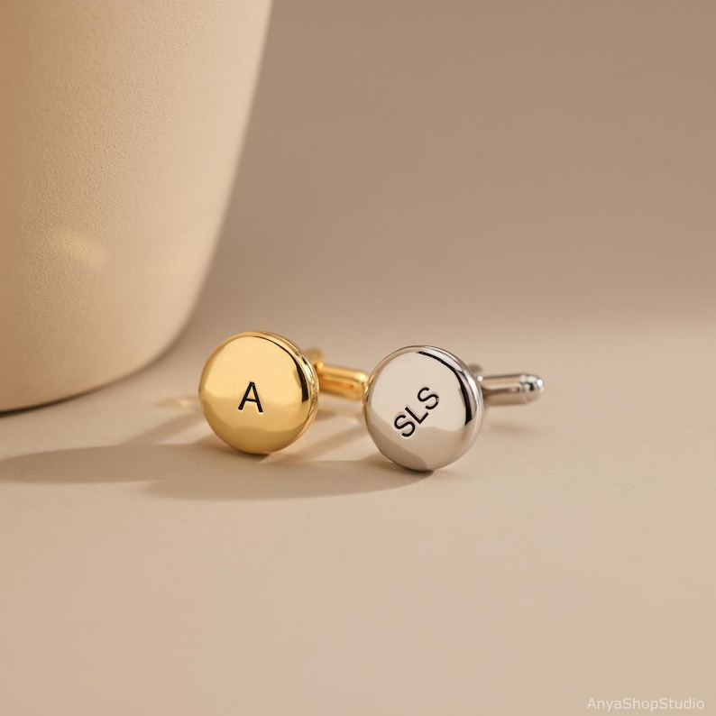 May include: Two round cufflinks with polished finishes. One cufflink is gold-toned and engraved with the letter A. The other cufflink is silver-toned and engraved with the letters SLS. Both feature a standard T-bar fastening mechanism.