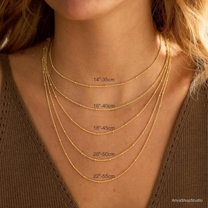 May include: Five gold-toned satellite chains of varying lengths, labeled with measurements from 14 inches to 22 inches. Each chain features small, evenly spaced round beads along the delicate link structure, displayed in a layered arrangement.