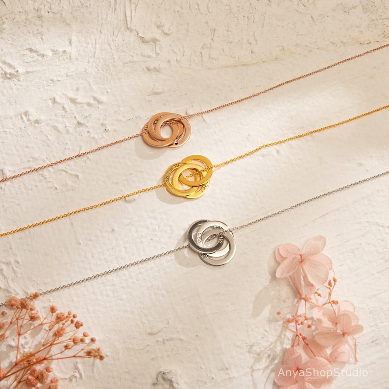 May include: Three interlocking gold rings on a chain necklace. The rings are engraved with the words "Forever", "Always", and "Love".
