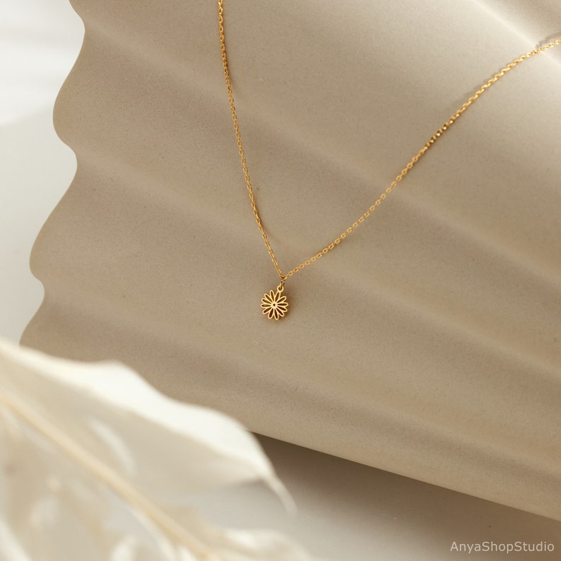 May include: A delicate gold chain necklace with a small, dainty flower pendant.