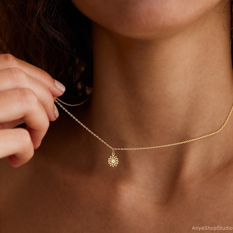 May include: A delicate gold chain necklace with a small, openwork daisy pendant.