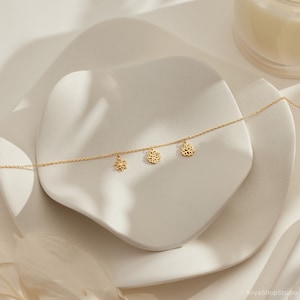 May include: A delicate gold chain necklace with three dangling charms: a small flower and two larger, intricate floral designs.