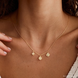 May include: A gold chain necklace with three delicate charms: a flower, a lotus, and another flower. The necklace is worn by a person with a light complexion.