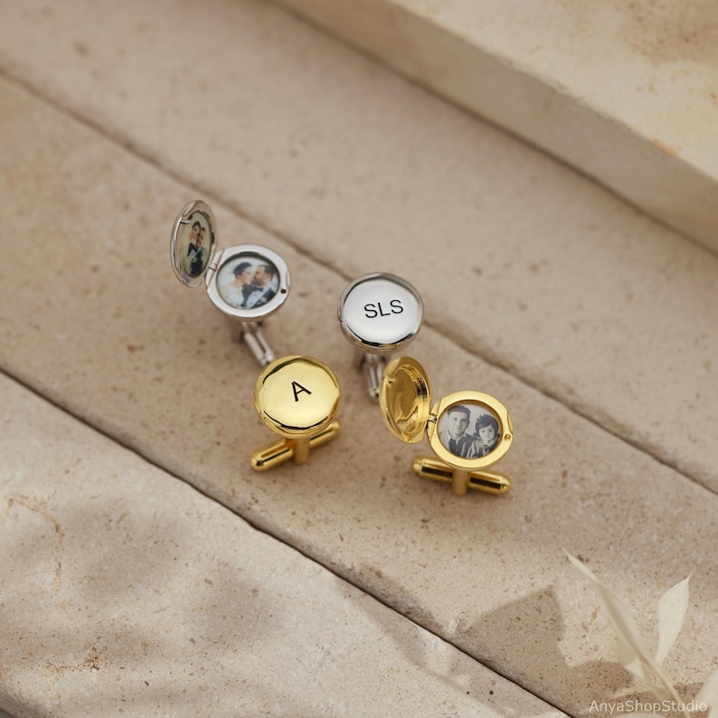 May include: A set of round metal cufflinks in gold and silver tones. Some cufflinks are closed, displaying the engraved letters A or SLS, while others are open, revealing small circular photographs of people inside the locket-style compartments.