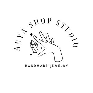 Könnte beinhalten: Anya Shop Studio Logo mit einer Hand, die einen Kristall mit Sternen um ihn herum hält. Der Text "Anya Shop Studio" befindet sich in einem Kreis um die Hand und den Kristall. Der Text "Handgemachter Schmuck" befindet sich unter dem Kreis.