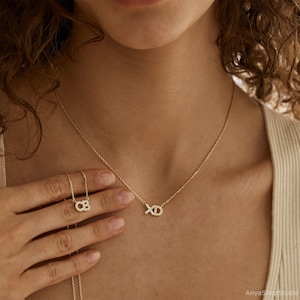 May include: A gold necklace with a delicate chain and a pendant that says "XO" in small, sparkling diamonds.