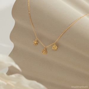 May include: A gold necklace with three delicate flower charms. The necklace is on a beige background.