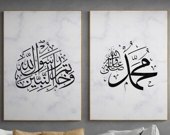 May include: Two framed canvas prints with black Arabic calligraphy on a white marble background. The prints are hanging on a gray wall above a gray couch with brown throw pillows.