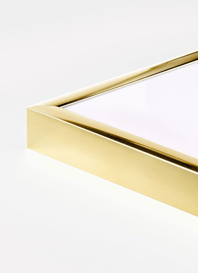 May include: Close-up of a gold picture frame with a smooth, polished finish. The frame is made of metal and has a simple, modern design.