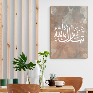 May include: A framed print with a white Arabic calligraphy design on a brown watercolor background. The calligraphy reads "Subhana Allahi wa bihamdihi".