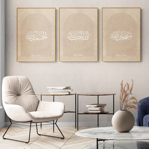Puede incluir: Tres impresiones enmarcadas con caligraf&iacute;a &aacute;rabe en blanco sobre un fondo beige. Las impresiones est&aacute;n dispuestas en fila en una pared beige claro. El texto de las impresiones dice "Allah Akbar", "Subhan Allah" y "Alhamdulillah".