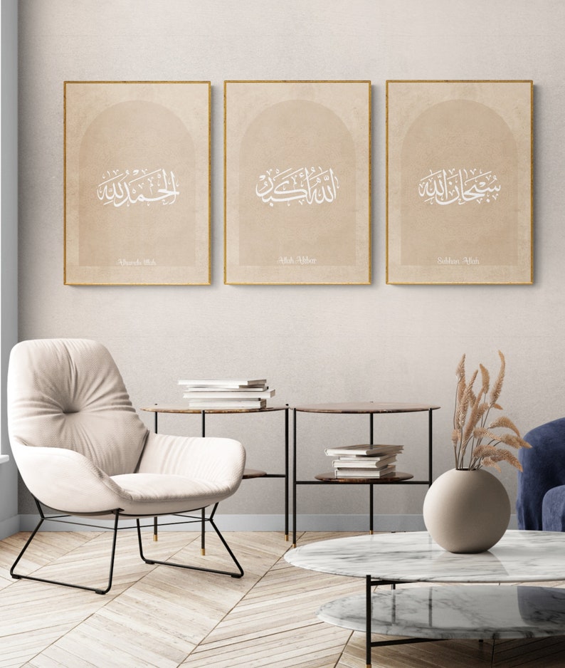 Puede incluir: Tres impresiones enmarcadas con caligraf&iacute;a &aacute;rabe en blanco sobre un fondo beige. Las impresiones est&aacute;n dispuestas en fila en una pared beige claro. El texto de las impresiones dice "Allah Akbar", "Subhan Allah" y "Alhamdulillah".