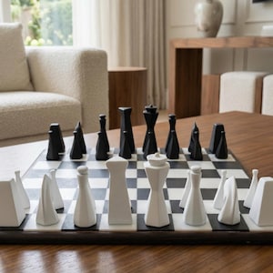 May include: A contemporary chess set with black and white pieces on a chequered board. The chess pieces have geometric designs. The board is on a dark wood table in a bright room.