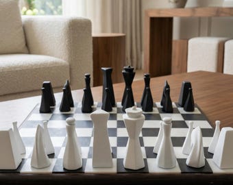 May include: A modern chess set with black and white pieces arranged on a checkered board. The chess pieces have geometric shapes. The board is set on a dark wood table in a living room setting.