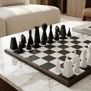 May include: A contemporary chess set featuring black and white pieces on a chequered board. The chess pieces are black and geometric, and the board has a dark wood frame. The board is on a marble table.