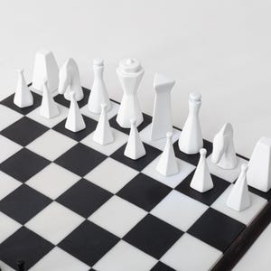 May include: A contemporary chess set featuring white pieces on a black and white chequered board. The chess pieces are minimalist, with geometric shapes and smooth surfaces. The board is framed in dark wood.