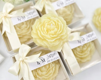Puede incluir: Conjunto de cinco cajas de regalo blancas con cinta de satén marfil y una sola vela en forma de flor marfil en cada caja. Las cajas están decoradas con una etiqueta personalizada con el texto "K&M Save the Date 09.18.2024".