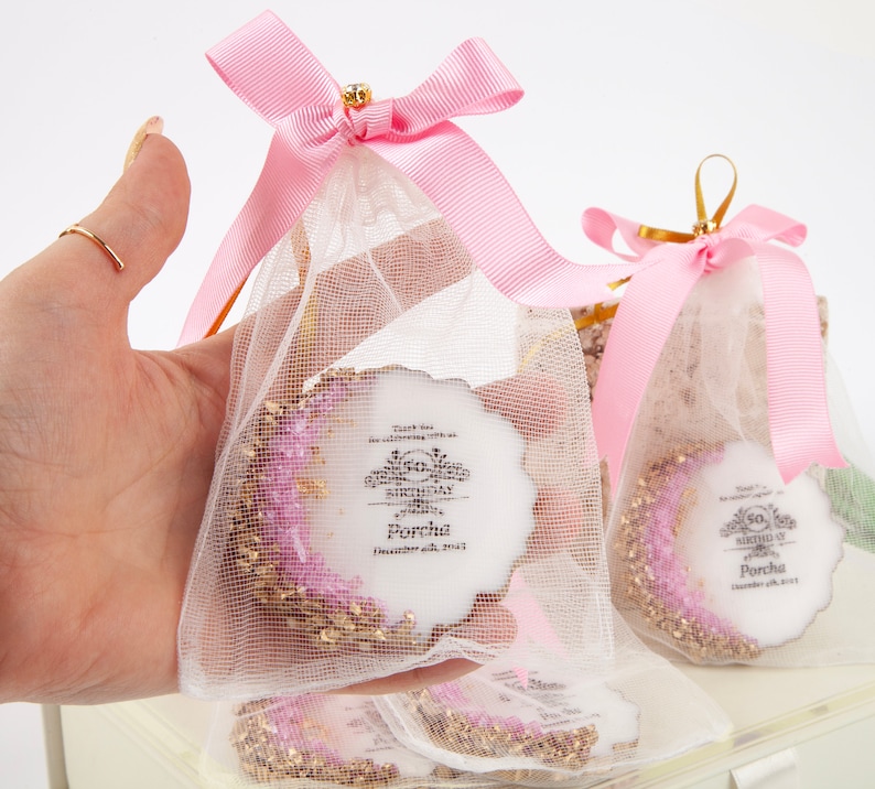 Puede incluir: Bolsas de regalo rosas y blancas con un adorno redondo de pastel blanco con purpurina dorada y un dise&ntilde;o rosa y blanco. El adorno de pastel tiene el texto "Thank you for celebrating with us on our 50th Birthday Porcha December 6th, 2023".