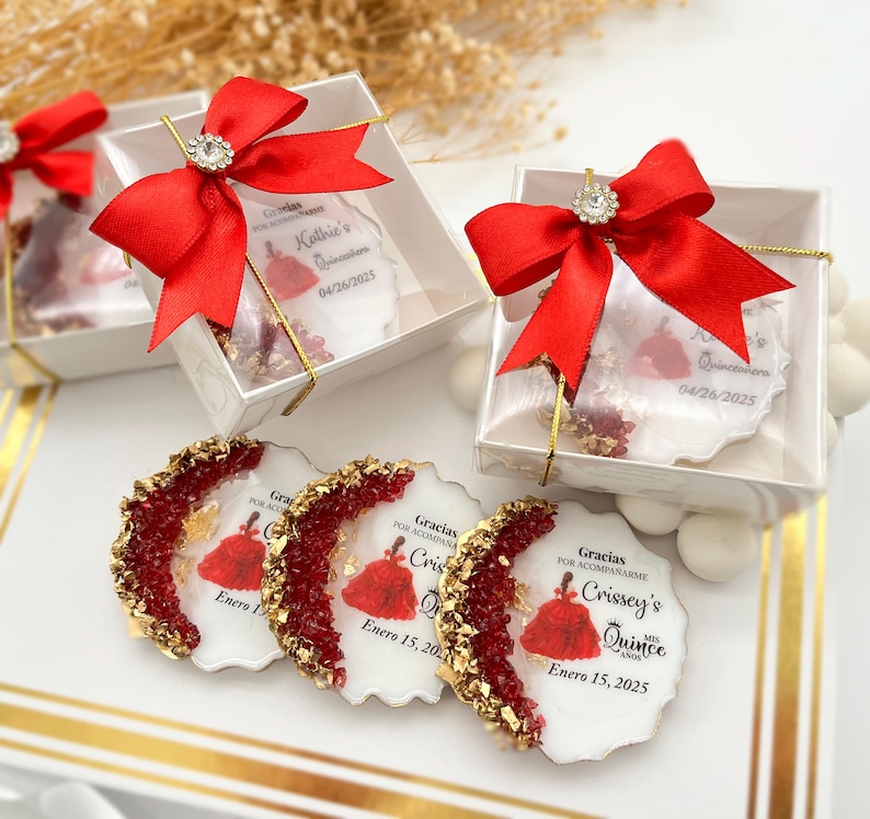 Op de afbeelding: Drie ronde witte onderzetters met rode en gouden glitteraccenten. Elke onderzetter heeft een gedrukte afbeelding van een vrouw in een rode jurk met de tekst "Gracias por acompa&ntilde;arme Crissey's Quince A&ntilde;os Enero 15, 2025".