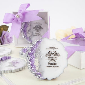 Puede incluir: Cajas de regalo moradas y plateadas con un inserto circular blanco que dice "Gracias por celebrar con nosotros. 50 cumplea&ntilde;os Porcha 4 de diciembre de 2023".