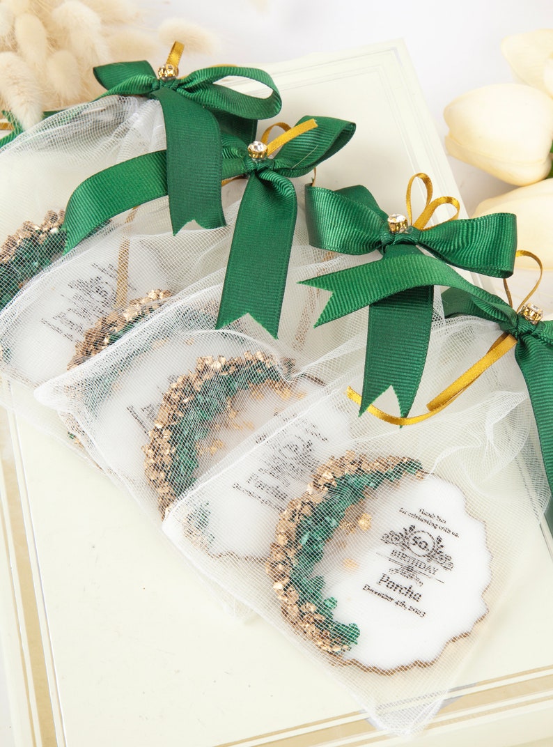 Puede incluir: Bolsas de regalo verdes y doradas con cintas de sat&eacute;n blancas y una etiqueta blanca con el texto "Gracias por celebrar con nosotros. Feliz cumplea&ntilde;os Parcha 4 de diciembre de 2023".