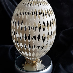 May include: A white ostrich egg carved with a diamond pattern, displayed on a silver stand with a mirrored top.