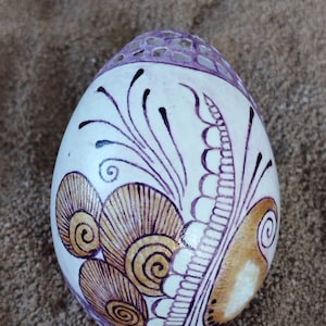 May include: A white egg with a purple and brown design. The egg is decorated with intricate swirls and patterns.