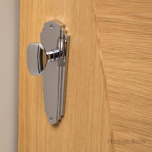 Könnte beinhalten: Ein polierter verchromter Türgriff mit einer quadratischen Rückplatte und einem abgerundeten Knauf. Der Griff ist an einer Holztür montiert.