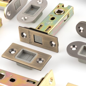 May include: Assortment of door latches in various metallic finishes, including gold, silver, bronze, and black. The latches have rectangular and oval faceplates with a square opening for the latch mechanism. The image showcases different styles and colors.
